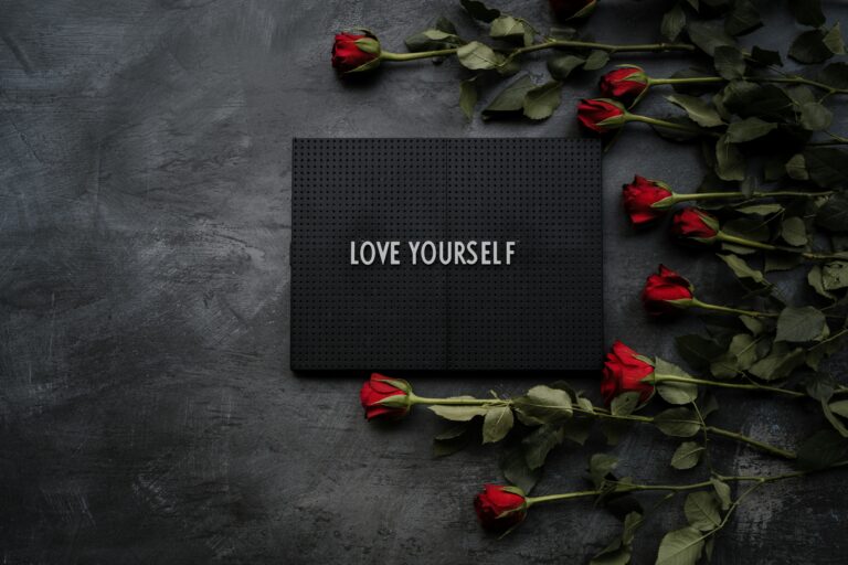 a black board with the words love yourself and a dozen red roses next to the board. This is self-love and mental wellness